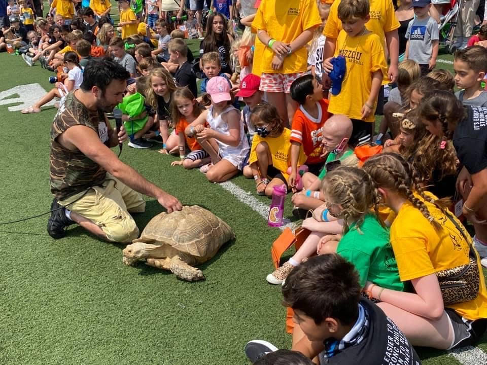 The team presenting a large reptile to an excited crowd of children
